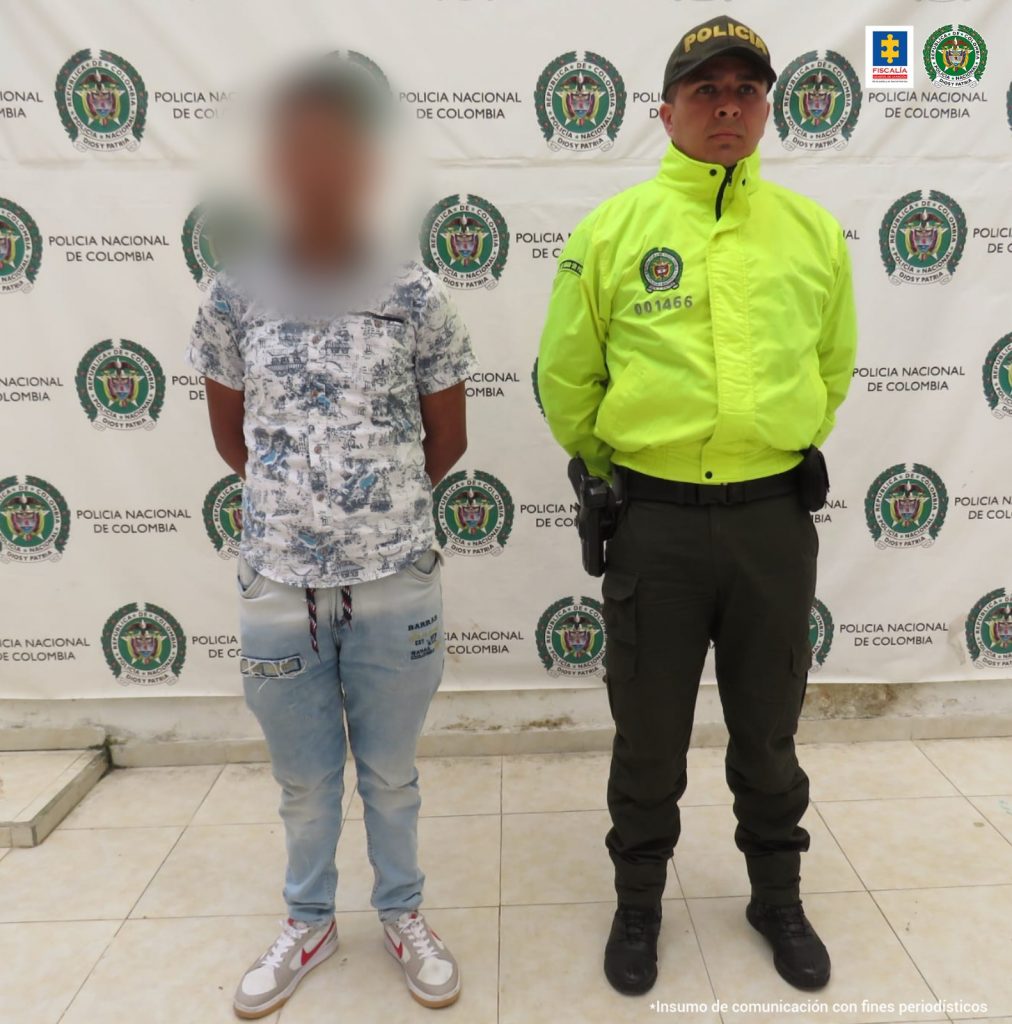 En la fotografía aparece un capturado, junto a personal de Policía Nacional. En la parte posterior de la imagen se ven banners de Policía Nacional y la Fiscalía General de la Nación.
