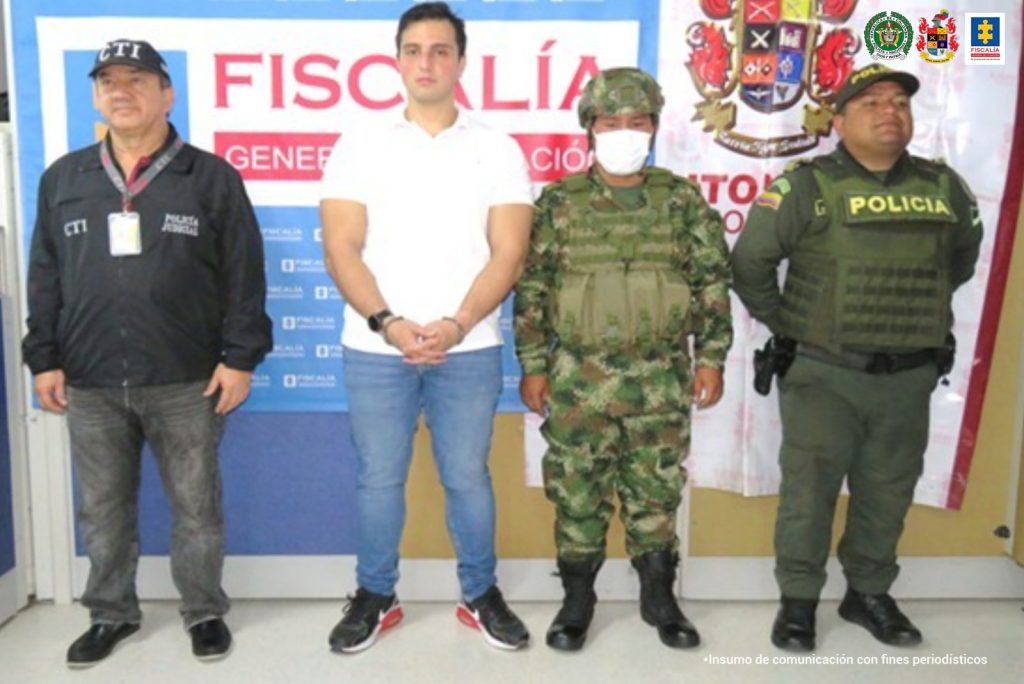 en la imagen se ve una persona detenida bajo custodia del CTI, Ejército y Policía. Detrás suyo backings institucionales de las dos primeras instituciones.