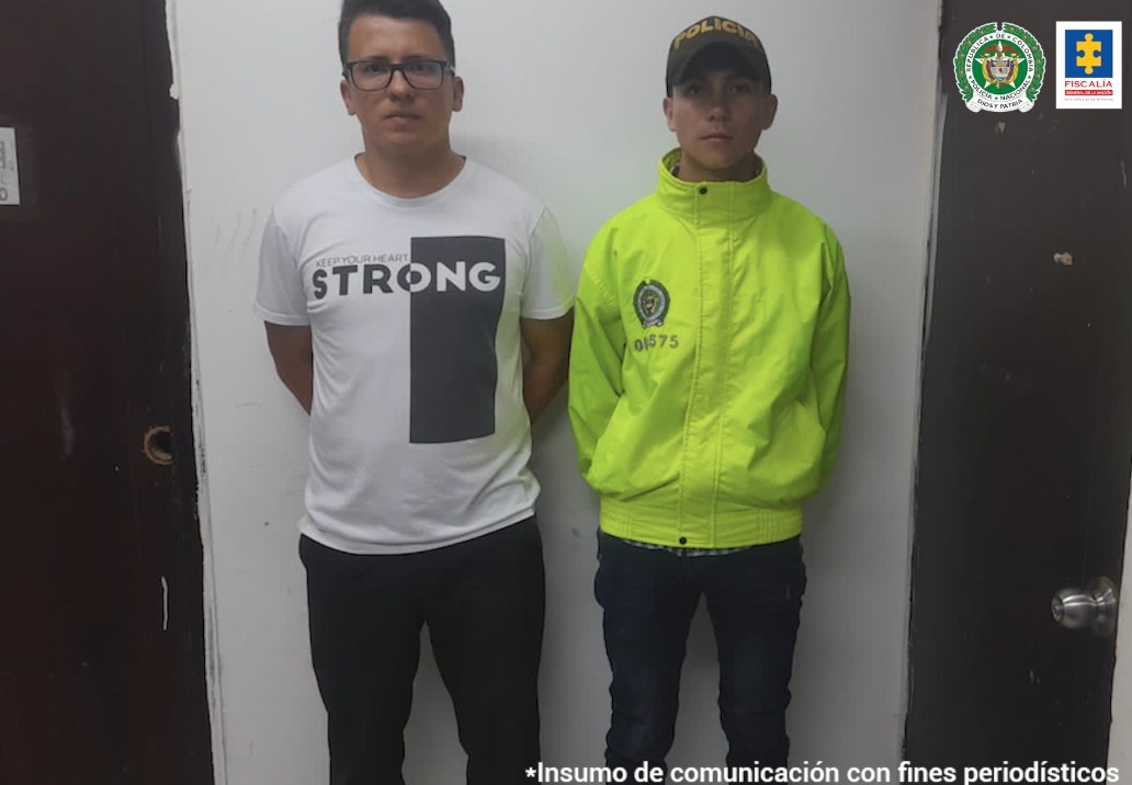 En la imagen se observa a un hombre de pantalón negro con camiseta blanca y negra al lado de un uniformado de la Policía Nacional.