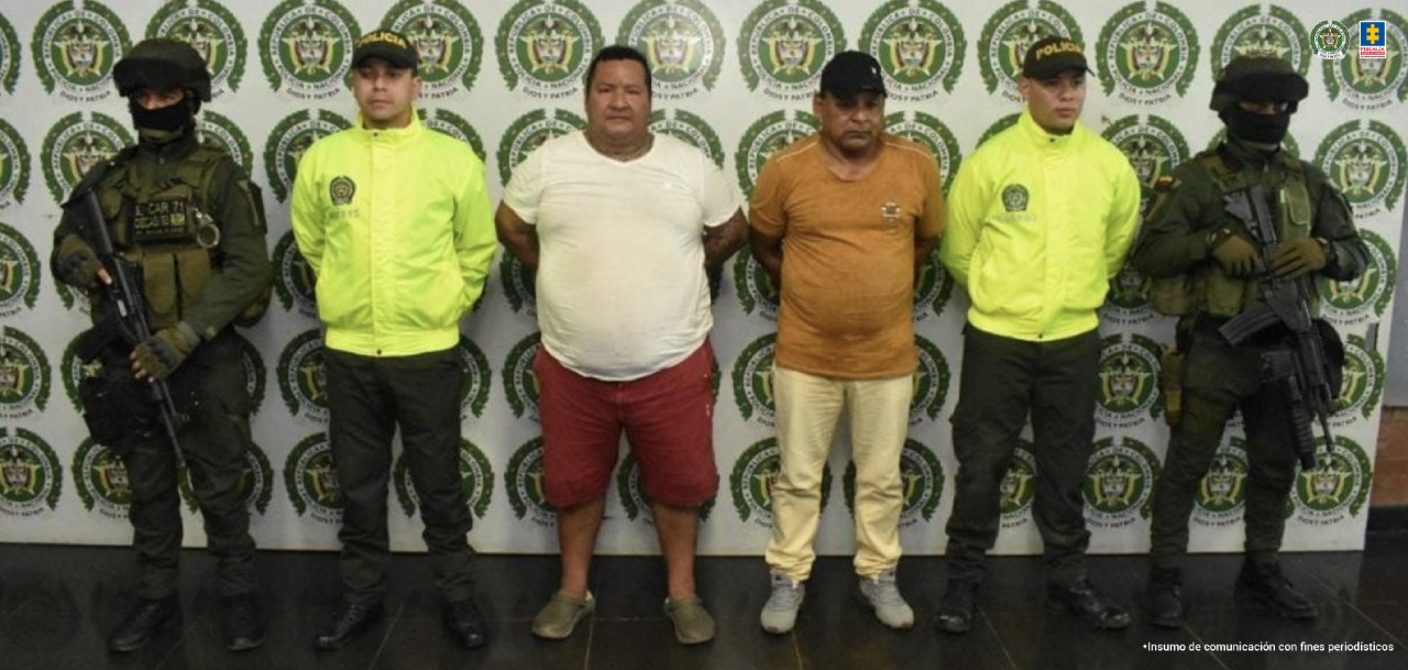 En la fotografía aparecen seis personas, dos de ellas son los capturados y los cuatro restantes integrantes de la Policía Nacional. De fondo se ve un baking con escudo de la Policía Nacional.