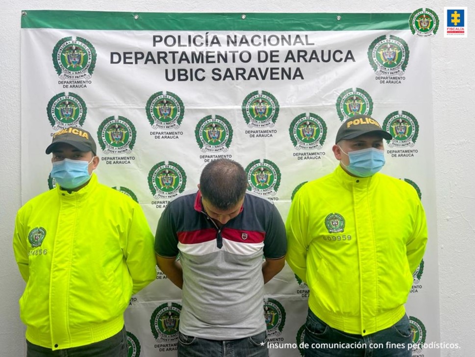 En la imagen se observa al capturado, junto a dos uniformados de la Policía Nacional. Detrás se ubica el banner que identifica a la Policía Nacional en Saravena (Arauca)
