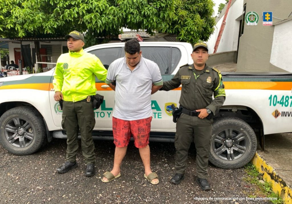 Se visualiza al capturado junto a dos uniformados de la Policía Nacional. Detrás de ellos una patrulla de la Policía Nacional.