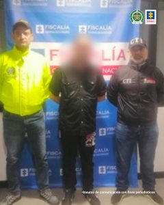 En la imagen se aprecia el capturado junto a un investigador del CTI y de la Policía Nacional, detrás el banner que identifica a la Fiscalía General de la Nación