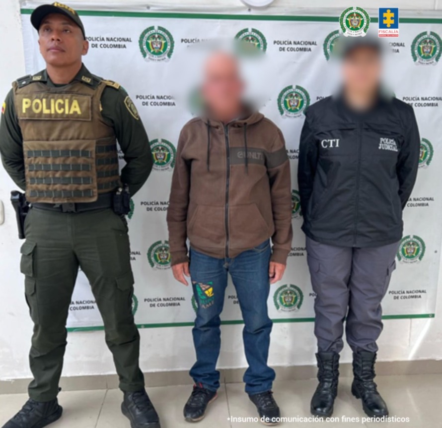 En la fotografía se aprecia de pie y con los brazos atrás, el hoy condenado. Viste con chaqueta de color marró, jean azul y zapatos negros. A su izquierda hay una servidora del CTI de la Fiscalía y a su izquierda hay un uniformado de la Policía Nacional. Detrás de ellos hay un pendón institucional de la Policía.
