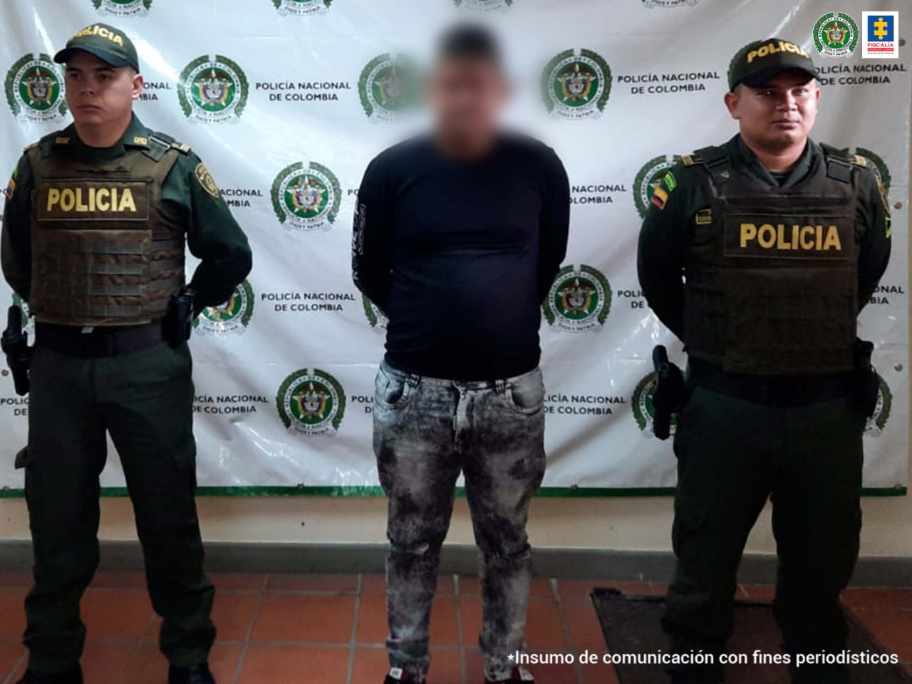 En la fotografía aparece un hombre capturado, junto a personal Policía Nacional. En la parte posterior de la imagen se obserban banners de Policía Nacional y la Fiscalía General de la Nación.