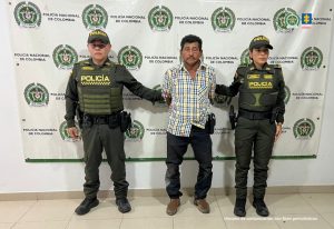 En la foto aparece el capturado de frente y custodiado por dos uniformados de la Policía Nacional. En la foto también aparece un backing de la Policía Nacional..