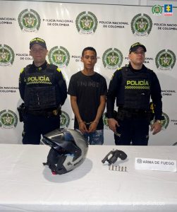 En la foto aparece el capturado custodiado por dos uniformados de la Policía Nacional. En la foto también aparece un backing de la Policía Nacional y el arma incautada.