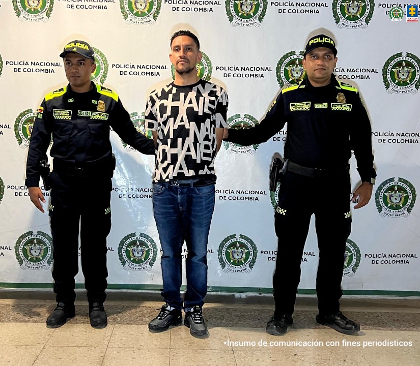 En la foto aparece el capturado en jean y un buso negro con letras blancas y custodiado por dos uniformados de la Policía Nacional. En la foto también aparece de fondo un backing de la Policía Nacional.