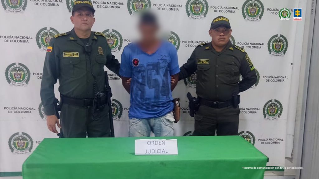 En la imagen aparece una persona de camiseta azul y jean, entre dos uniformados de la Policía.