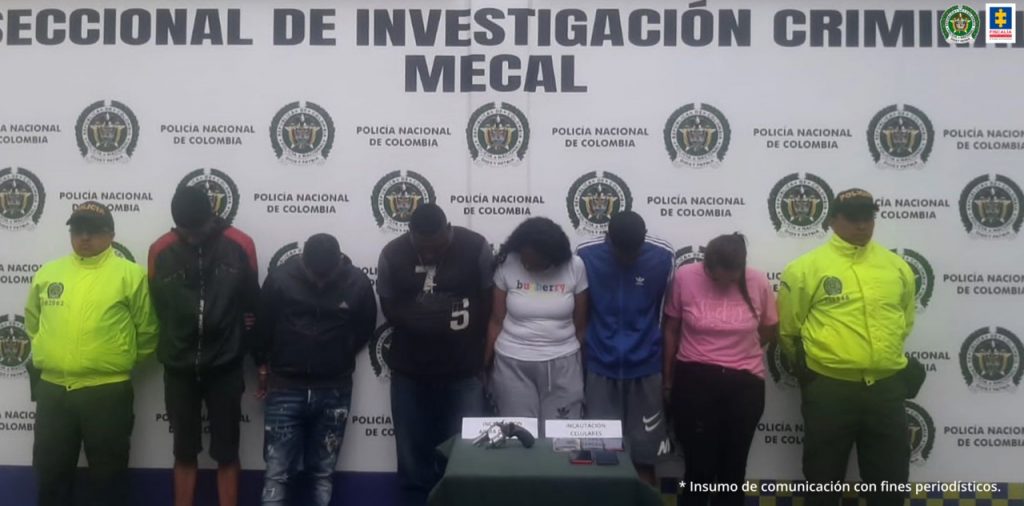 En la fotografía aparecen 6 personas capturadas, entre ellas dos mujeres junto a dos agentes de la Policía Nacional. En la parte posterior de la imagen se ve un banner de la Policía Nacional.