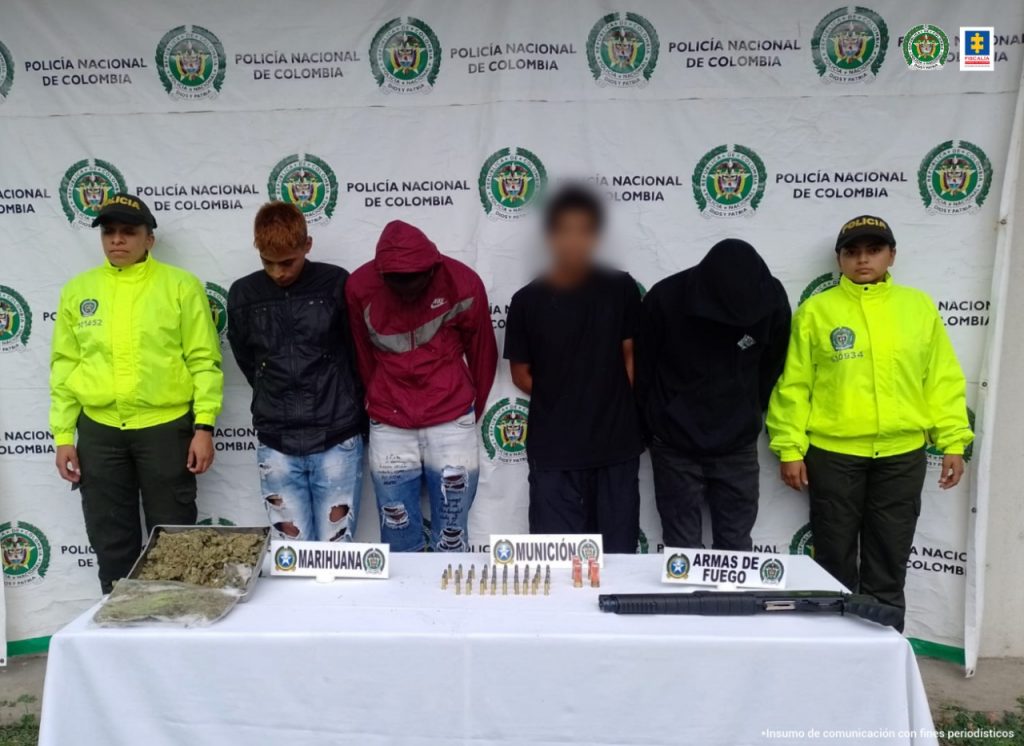 En la fotografía aparecen tres hombres capturados, junto a dos agentes de la Policía Nacional. En la parte posterior de la imagen se ve un banner de la Policía Nacional