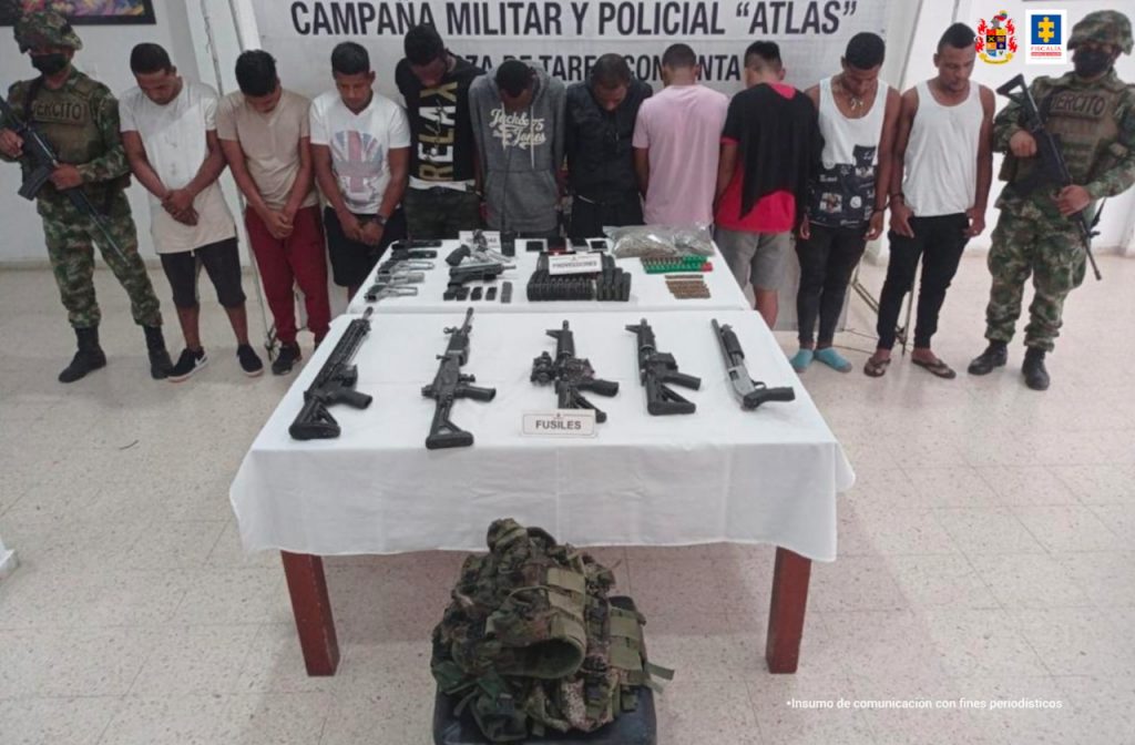 En la fotografía se observan 8 de los capturados con dos menores de edad, junto a dos soldados de la Fuerza de Tarea Hércules. En la parte posterior se observa una mesa con fusiles, pistolas, munición, un radio de comunicación, entre otros elementos. 