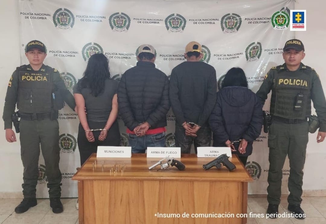 En la fotografía se observan a los 4 capturados junto a agentes de la Policìa Nacional. En la parte posterior se observa una mueble con dos armas de fuego y municiones.