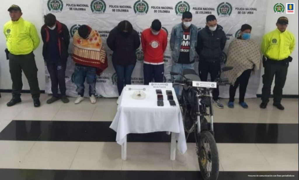 En la fotografía se observan a los 7 capturados junto a dos agentes de la Policía Nacional. En la parte posterior se observa una mesa con 6 teléfonos celulares, marihuana y una motocicleta