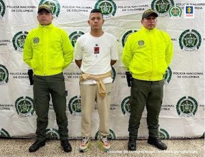 Dos uniformados de la Policía Nacional custodian al procesado, de camisa blanca, quien está esposado.
