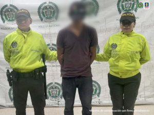 Los capturados están custodiados por uniformados de la policía nacional, esposados y con un pendón institucional detrás de ellos.