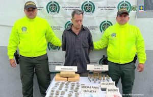 En la imagen se ve una mujer y dos hombres detenidos bajo custodia de dos integrantes del Gaula de la Policía Nacional. Detrás suyo un backing institucional.