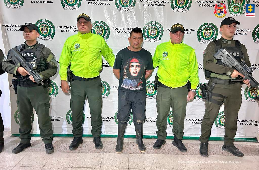 El capturado aparece en el centro de la imagen, esposado con las manos atrás. Lo rodean miembros de la fuerza pública.