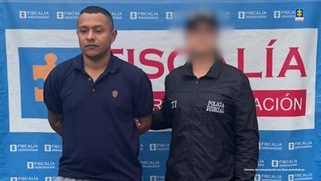 Andrés Felipe Moreno Villada, señalado de homicidio, acompañado por un funcionario del CTI de la Seccional Caldas. Al fondo el pendón con logos de la Fiscalía.