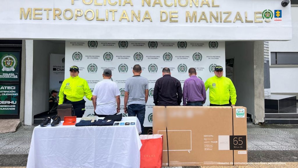 En la fotografía se ve a cuatro hombres identificados como Fabio Rojas Zuluaga, José Lifer Pérez Morales, Carlos Ariel Díaz Noreña y Alex Mauricio Rodríguez acompañados de policías y al fondo un pendón de la Policía. En una mesa los artículos que habrían logrado conseguir a través de créditos con documentos falsos.