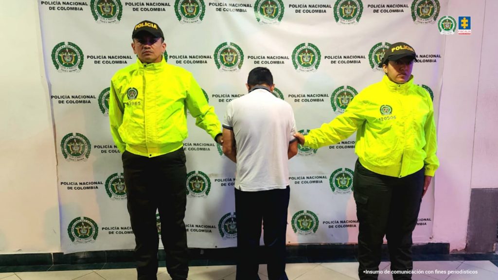 En la foto aparece el pastor religioso acompañado por dos funcionarios de la Policia Nacional y atrás un pendón con logos de la misma institución.