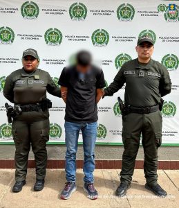 Capturados de frente custodiados por policías. Detrás banner de la Policía Nacional.