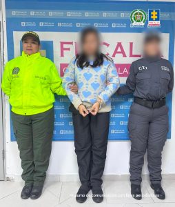 capturada de frente custodiada por investigadora del CTI de la Fiscalía y mujer policía. Detrás banner de la Fiscalía General de la Nación.