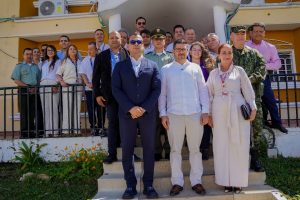 En la foto aparece un grupo de personas entre hombres y mujeres, vestidos de colores claros y un hombre de traje azul con gafas oscuras. En unas escaleras.