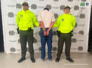 El procesado quien está de espaldas y esposado, es custodiado por dos uniformados de la Policía Nacional.