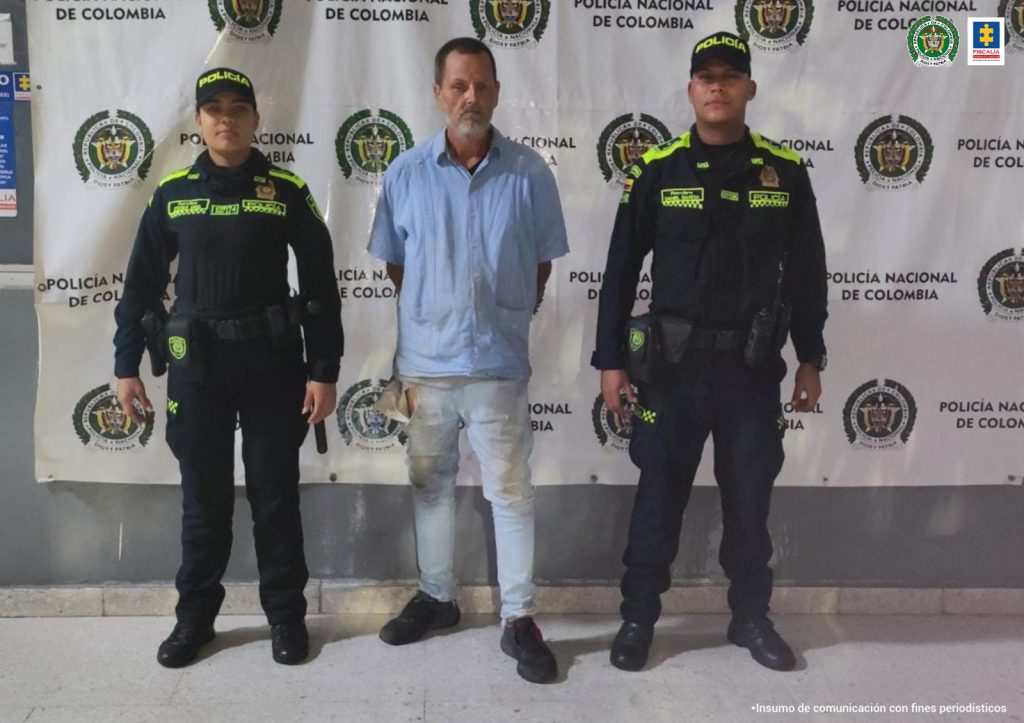 El procesado tiene una camisa blanca y está esposado. Uniformados de la Policía Nacional lo custodian.