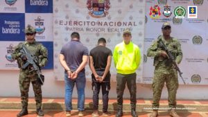 Los dos capturados aparecen esposados con sus manos, están de espalda y protegidos por miembros de la policía y el ejército.