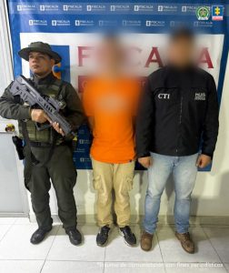 En la fotografía aparece el capturado junto a un funcionario del CTI y un uniformado de la Policía Nacional. En la parte superior está un banner de la Fiscalía General