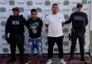 En las fotografías se observan los tres capturados juntos a dos agentes del Guala Policía y dos soldados del Ejército Nacional. En la parte superior están tres banner de la Fiscalía General, un banner del Ejército Nacional y un banner de la Policía.