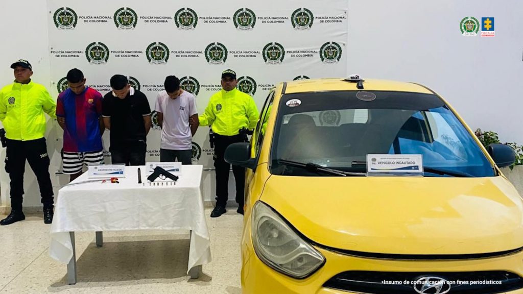 En la fotografía aparecen tres hombres capturados en compañía de dos uniformados de la Policía Nacional. En la parte posterior un banner con logos de la entidad.