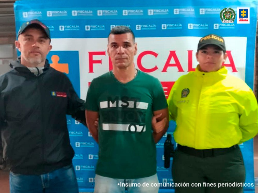 Se observa el capturado y a cada lado un funcionario de CTI y uno de la Policía. Atrás backing de la Fiscalía