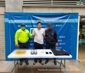 En la imagen está el procesado en medio de un servidor del CTI y otro de la Policía Nacional con una mesa al frente con los elementos incautados