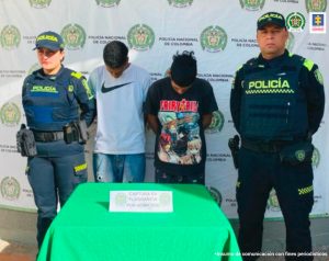 Se observan los dos capturados de frente y a cada costado un funcionario de Policía Nacional. Al fondo un pendón de Policía Nacional.