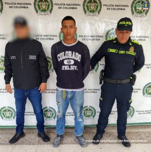 En la foto aparecen el capturado con buso negro de frente y custodiado por un servidor del Cuerpo Técnico de Investigación CTI y la Policía Nacional. En la foto aparece un backing de la Policía Nacional.