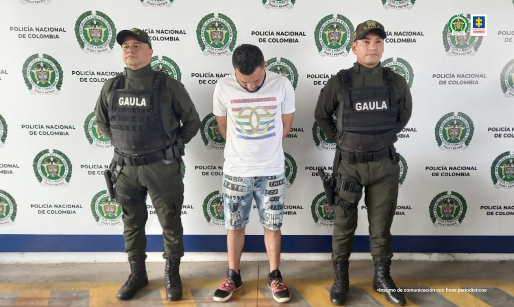 Se observa al capturado y a cada costado un funcionario de Policía Nacional. Atrás un pendón de Policía Nacional
