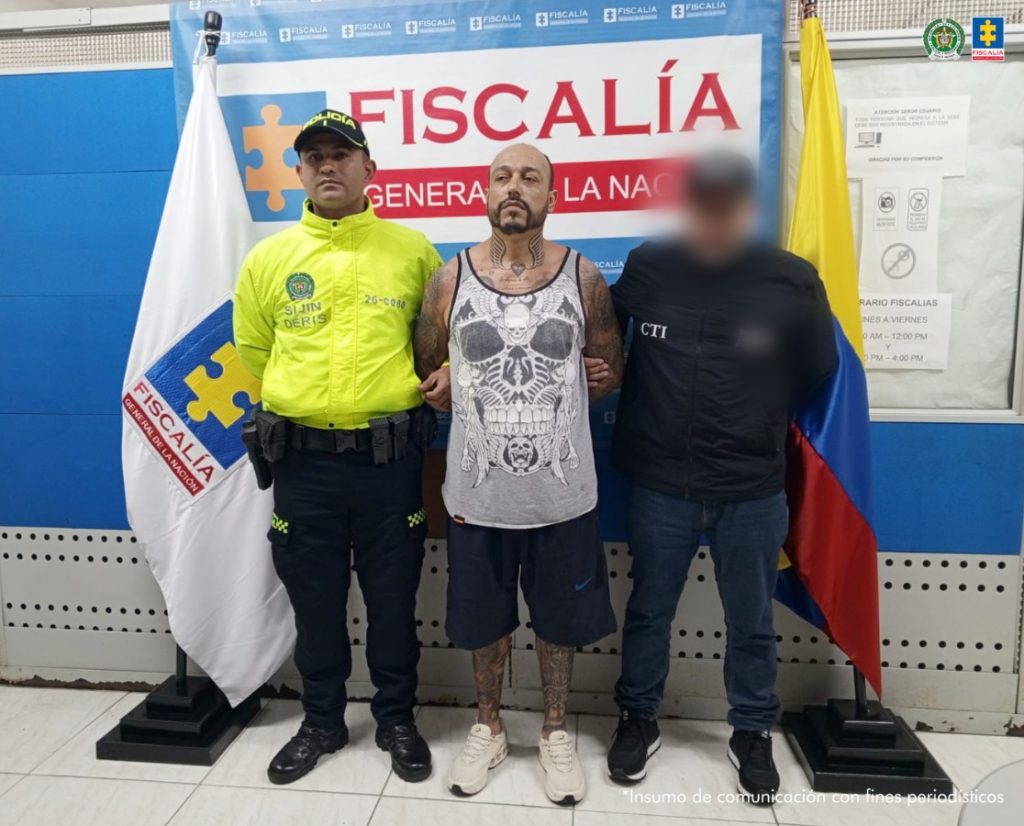 Se observa al capturado de frente en medio de un funcionario de l CTI y otro de Policía Nacional. Atrás, un pendón de Fiscalía General de la Nación