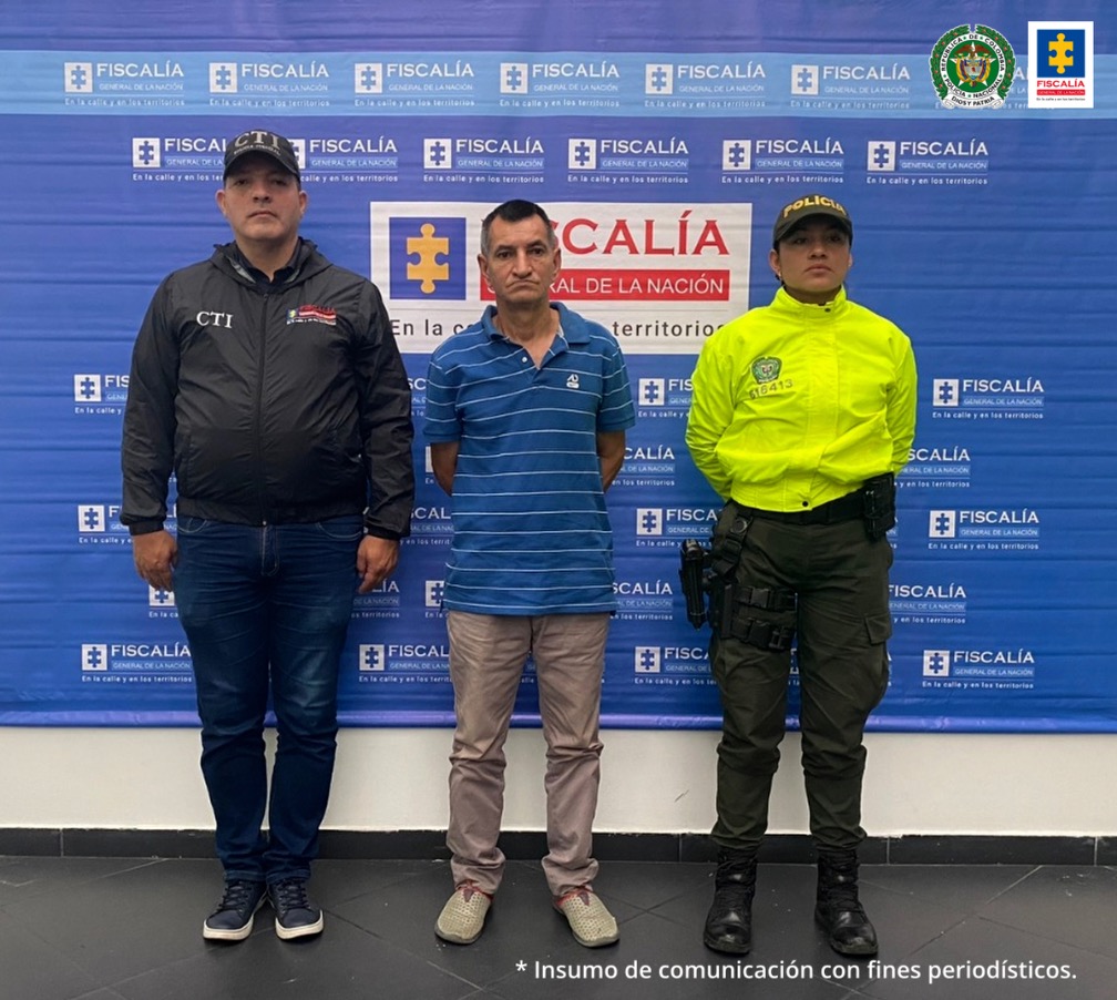 El capturado aparece frente a un banner de la Fiscalía General de la Nación, junto a personal de la Fiscalía y la Policía.