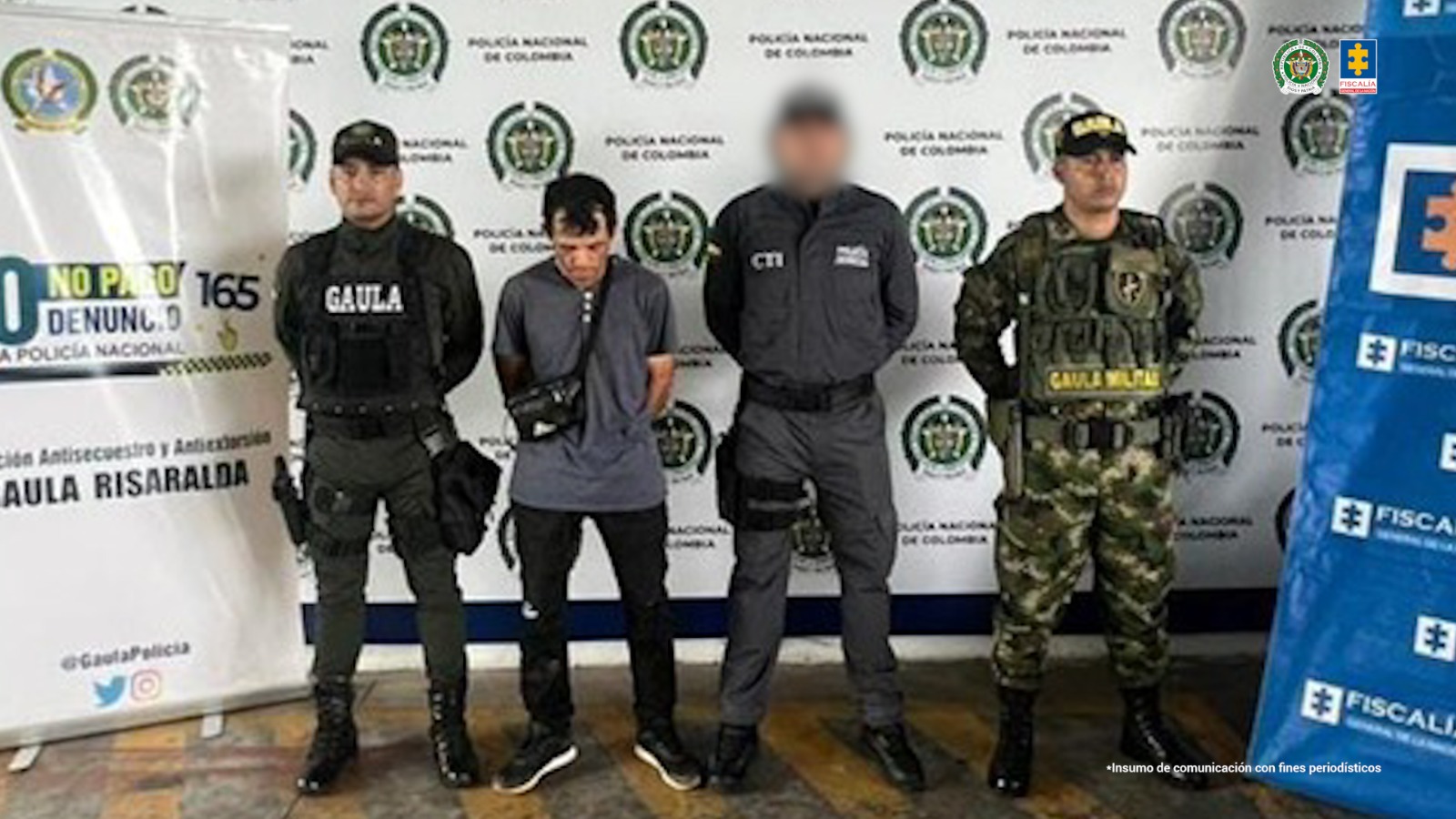 se observa al capturado y lo custodian un funcionario del CTI, otro de Policía y otro de Ejército. Atrás un pendón de Policía, al lado uno de Ejército y otro de Fiscalía General de la Nación