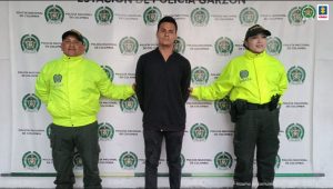 en la imagen se ve una persona detenida bajo custodia de dos integrantes de la Policía Nacional. Detrás suyo un backing institucional.