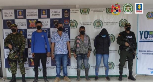 en la imagen se encuentran cuatro personas detenidas bajo custodia del Ejército y Policía Gaula. Detrás suyo, backings institucionales. 