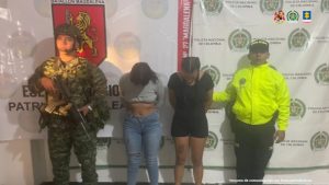 Las imputadas se encuentran en custodia por un uniformado del Ejército y Policía Nacional. Detrás hay un backing de la Policía Nacional.