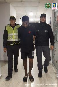 En la foto se aprecia en acción de caminata y con los brazos atrás a Jaider Montaño. Viste con camiseta negra de manga corta; pantaloneta negra y pantuflas negras. Al lado izquierdo de él hay un servidor del CTI de la Fiscalía y al lado derecho un uniformado de la Policía Nacional.