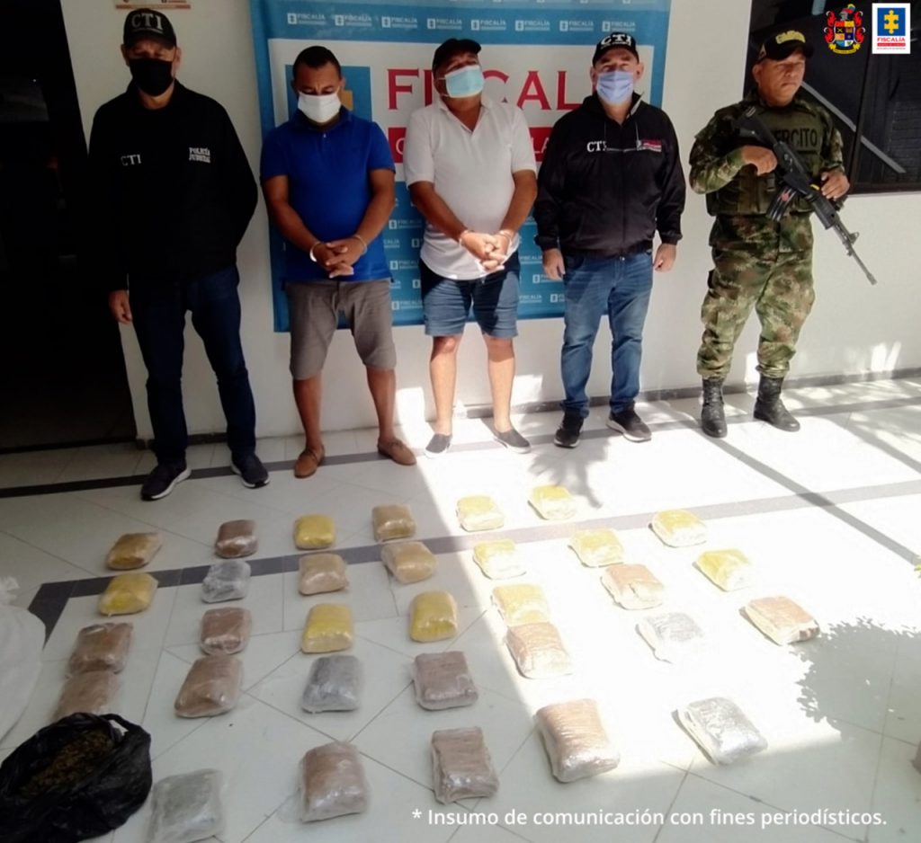 En la fotografía aparecen dos hombres capturados, junto a personal de la Policía Nacional, el Ejército y el CTI. En la parte posterior de la imagen se ve un banner de la Fiscalía General de la Nación.
