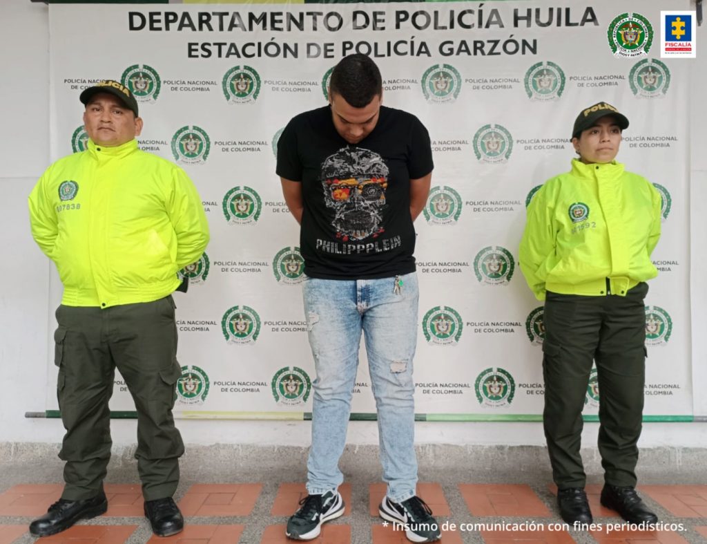 En la fotografía aparece un capturado, junto a personal de Policía Nacional y Fiscalía General de La Nación. En la parte posterior de la imagen se ven banners de Policía Nacional y la Fiscalía General de la Nación.