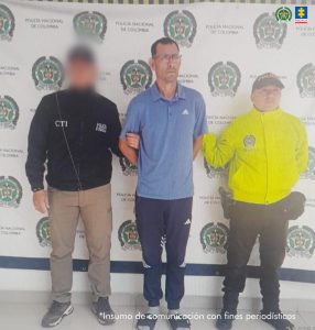 En la fotografía aparece de pie y con los brazos atrás Jair Arnulfo Cortés Morales. Viste con camisa de color azul, mangas cortas, de cuello, con estampado blanco en el lado izquierdo del pecho; así como pantalón de sudadera de color azul oscuro, con franjas blancas laterales a la altura de las rodillas; medias grises y pantuflas azules. En le extremo derecho del imputado hay un servidor del CTI de la Fiscalía y en el izquierdo hay una unidormada de la Policía Nacional. Detrás de ellos hay un pendón institucional de la Policía.