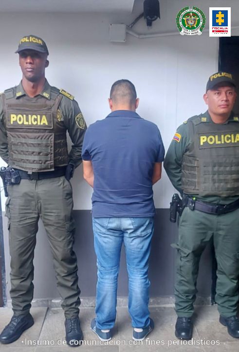 En la fotografía aparece de espaldas a la cámara y con los brazos adelante Jairo Ubaner Díaz Guerrero. Viste camiseta de manga corta color azul y jean azul. Al lado y lado de él hay uniformados de la Policía Nacional.